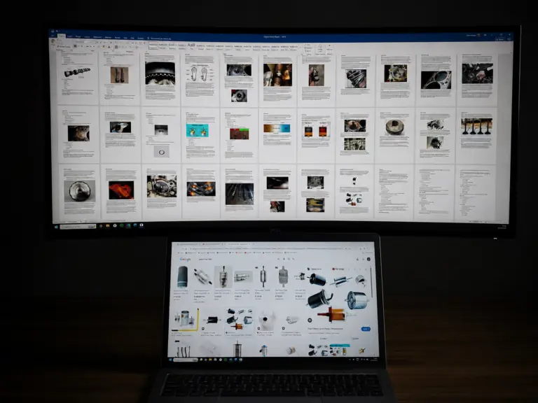 Automotive engine failure analysis reports and mechanical component research displayed on dual-screen workstation